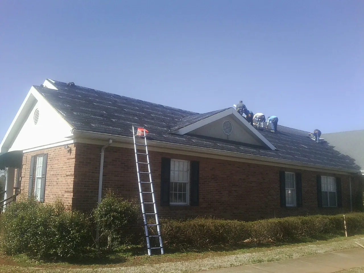 Crew tearing shingles off a brick ranch roof with a ladder set — Metal Roof Repair work by our crew in Great Valley