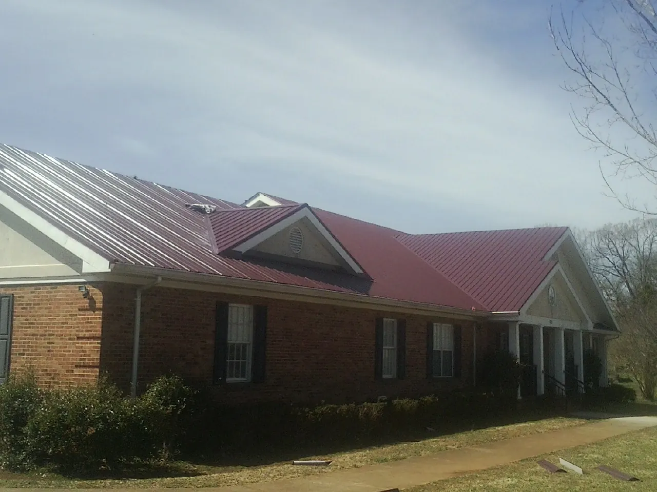 Red metal roof with gabled entries on a long brick building, from a Hail Damage Roof Repair job in Great Valley