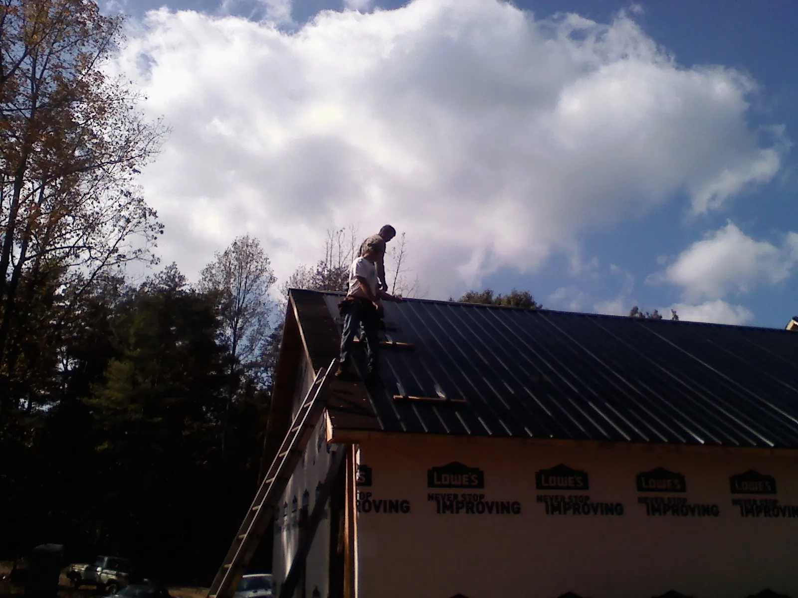Roofer fastening dark metal panels high against a cloudy sky, from a Roof Inspection job in Great Valley