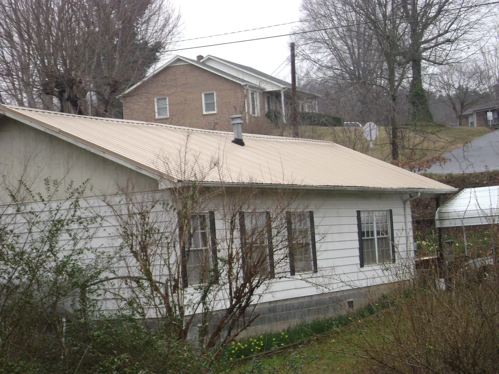 Tan metal roof on a white sided house set into a hillside — Commercial Roofing by Roofing Brothers in Great Valley